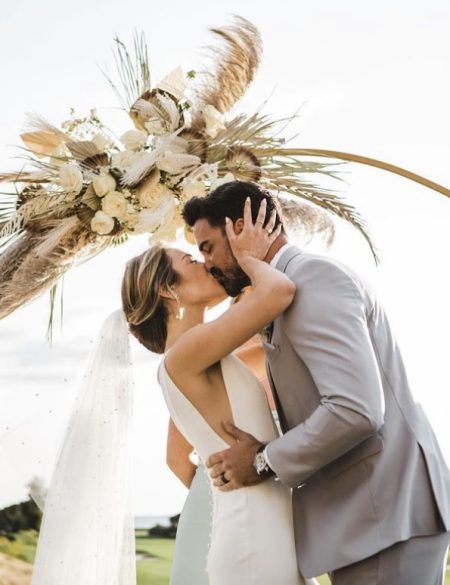 bride and groom in front of wedding arch decorated in pastel wedding flower arrangement